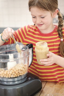 A young girl spooning ingredients into a food processor