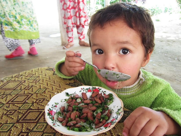 Child in Tajikistan eating a bowl of beans