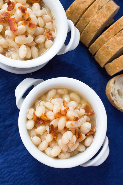 Carmy's Tuscan Bean Soup with bacon crumbled on top and a loaf of bread in the background