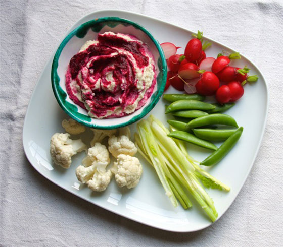 A bowl of hummus on a plate with veggies